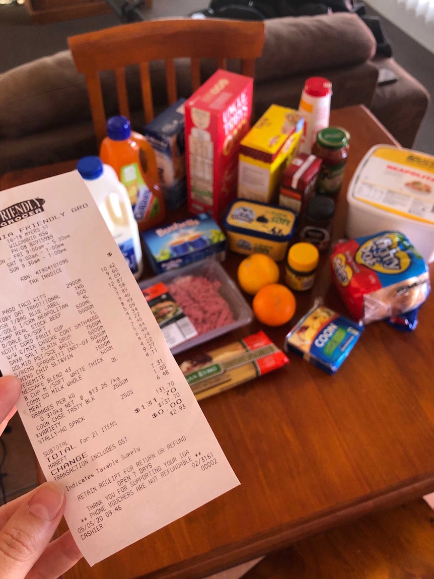 A receipt from a supermarket totalling $131.70 with a table full of groceries in the background.