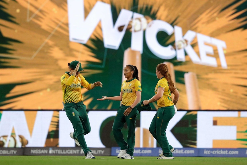 A trio of cricketers celebrate as the word "Wicket" on a big scoreboard at the Women's T20 WorldCup