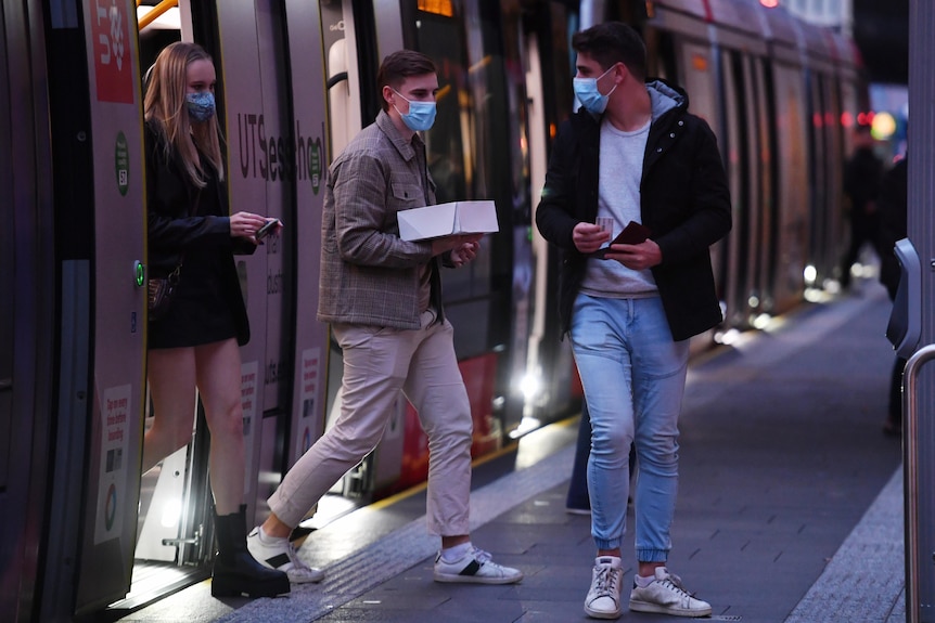 a group of young people hopping off a tram wearing face masks