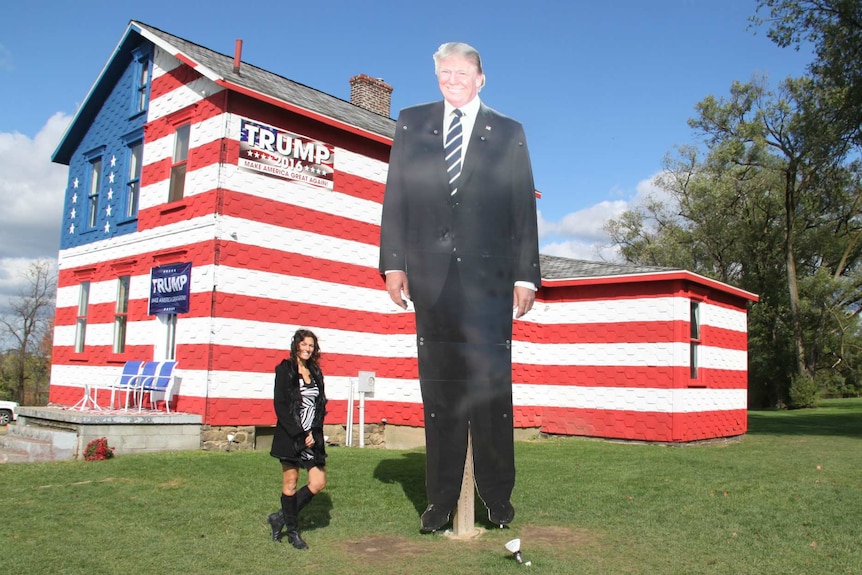 Leslie Baum Rossi stands next to a giant Trump placard