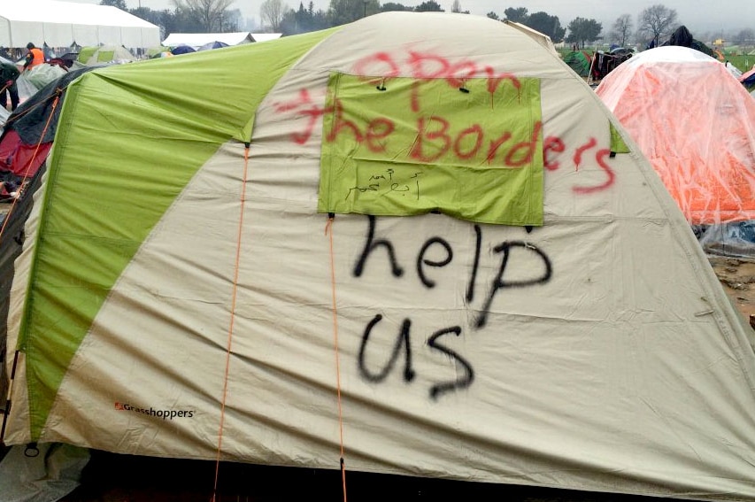 The message - open the borders, help us - spray painted on the side of a tent at the Idomeni refugee camp.