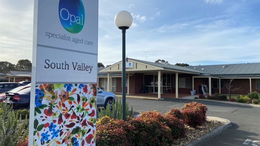 A sign reading 'Opal specialist aged care' stands in front of a single-storey red brick building.