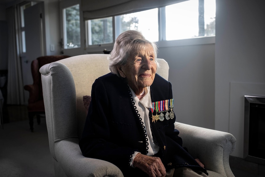 An elderly woman wearing war medals sitting in an armchair.