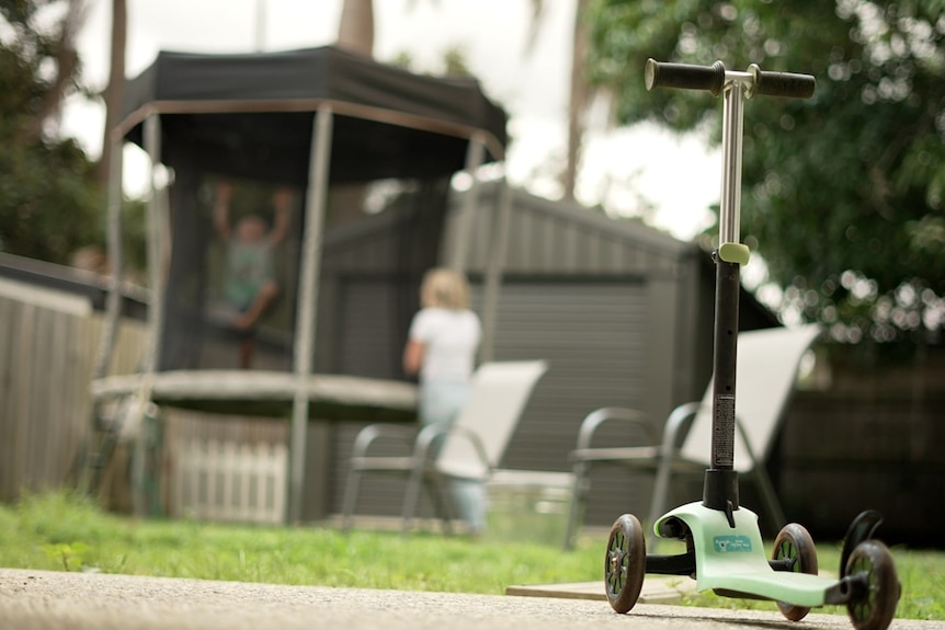 A children's scooter, with a trampoline in the background.