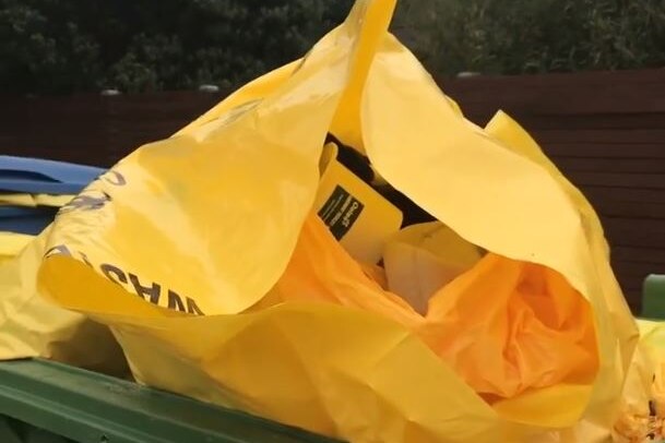 A yellow bag of medical waste sits open in a green skip.