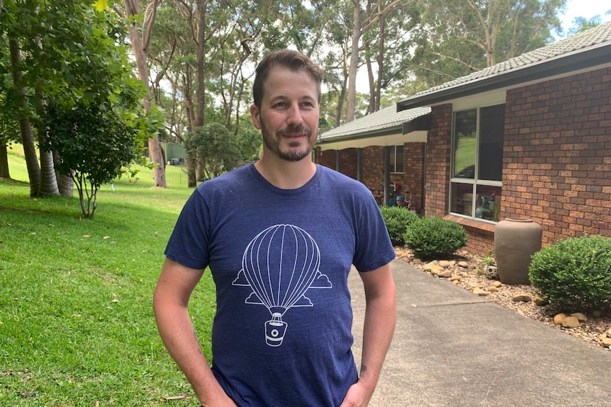 Man with hands in pockets standing outside a brick house