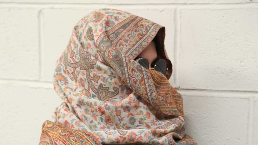 A woman wearing a headscarf and sunglasses looks away from the camera