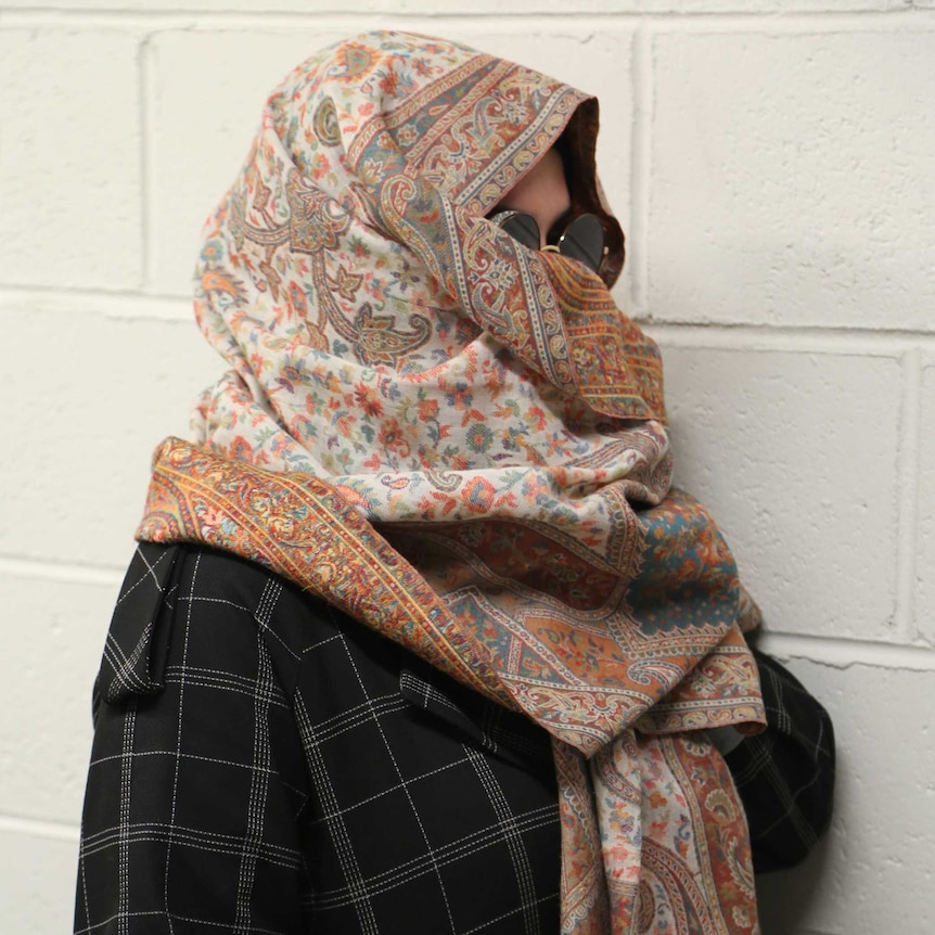 A woman wearing a headscarf and sunglasses looks away from the camera