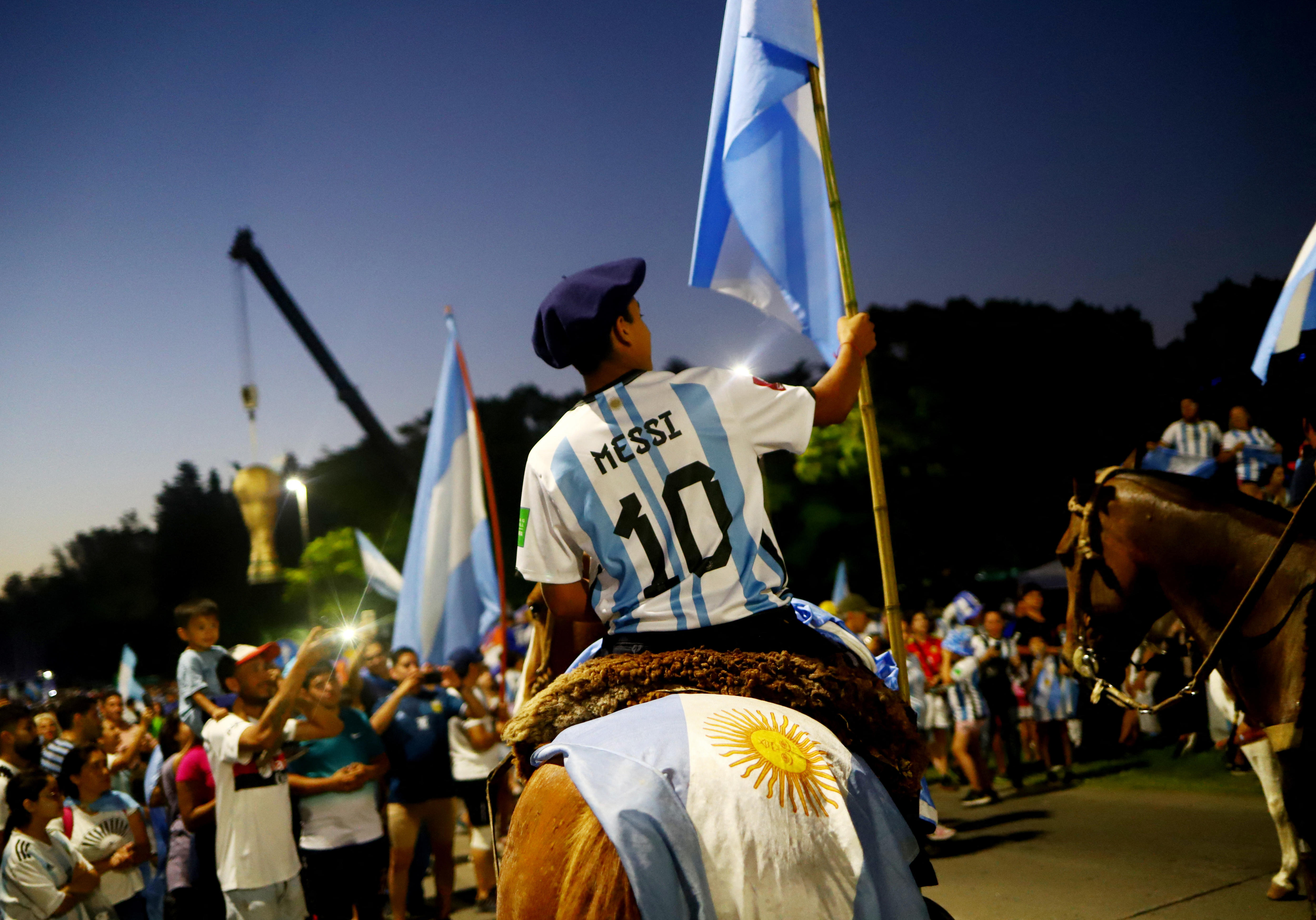 A perosn in a Messi jersey rides a horse waving an Arigentinian flag. 
