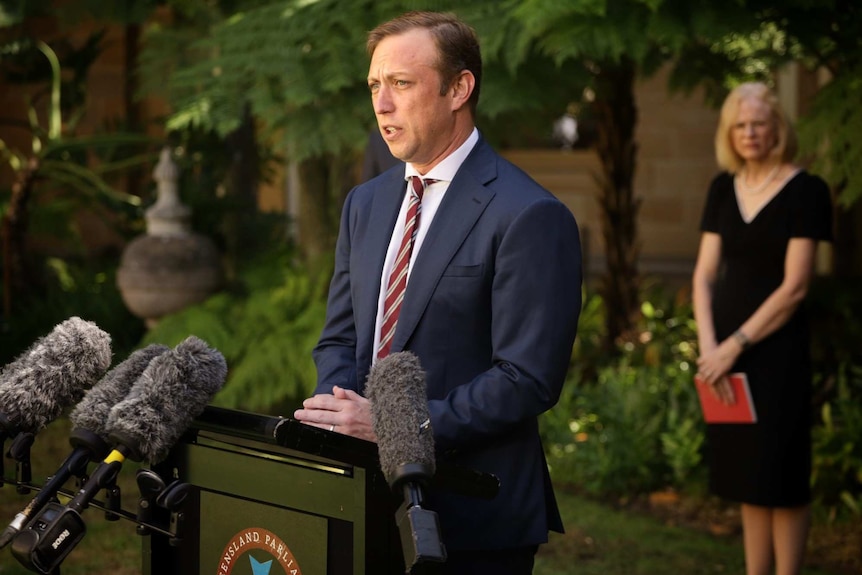 Queensland Health Minister Steven Miles, with Dr Jeannette Young behind him, speaks at a media conference.