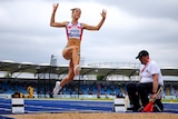 A female long jumper is pictured in mid jump with arms out and legs at full stretch above the sand. 