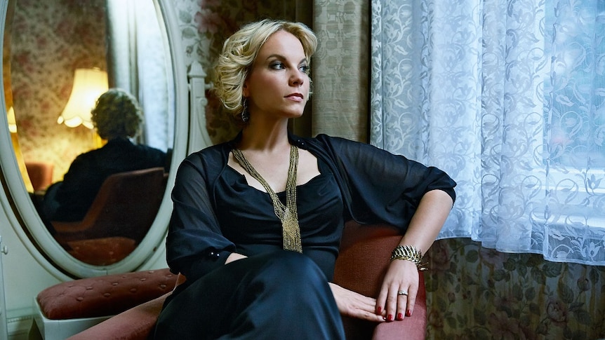 Mezzo-soprano Elīna Garanča seated, gazing out a window, a mirror behind her.