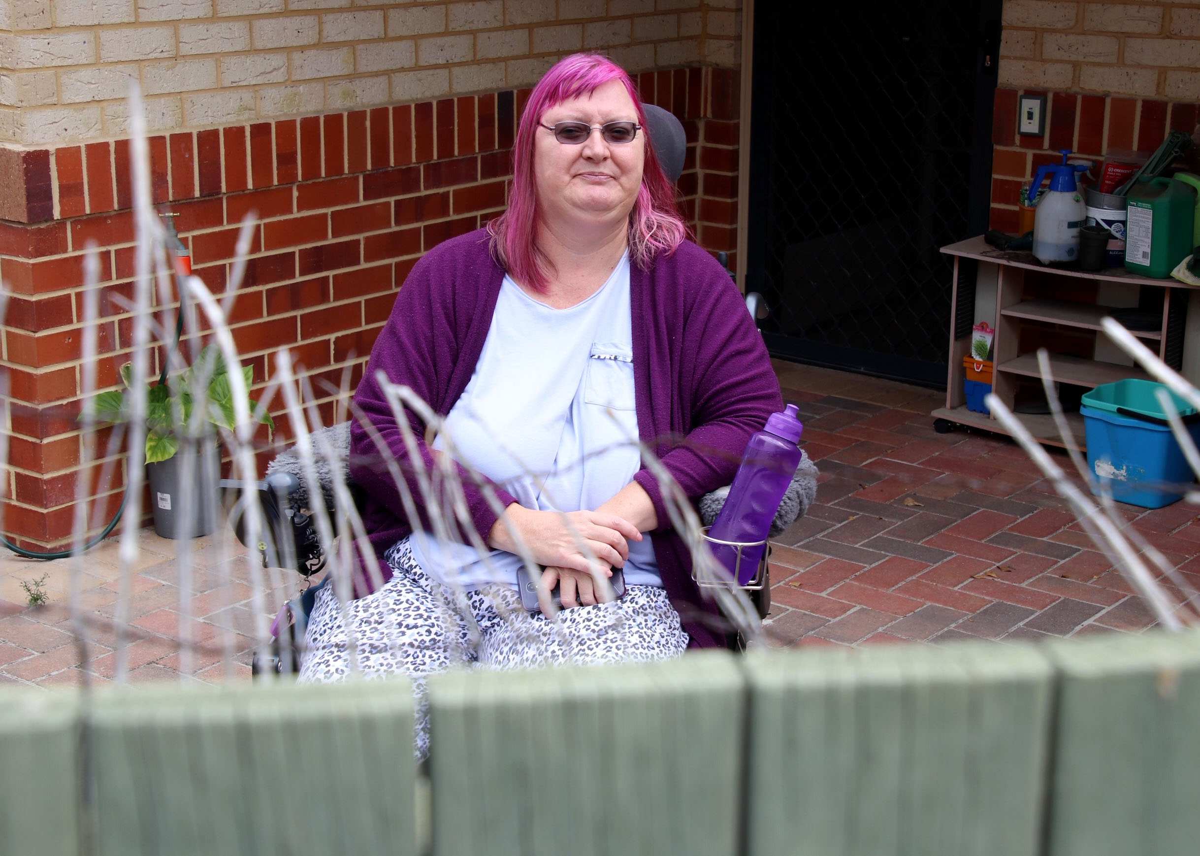 Ms Lamb sits in a wheelchair and looks over her fence towards the camera.