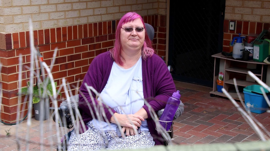 Ms Lamb sits in a wheelchair and looks over her fence towards the camera.