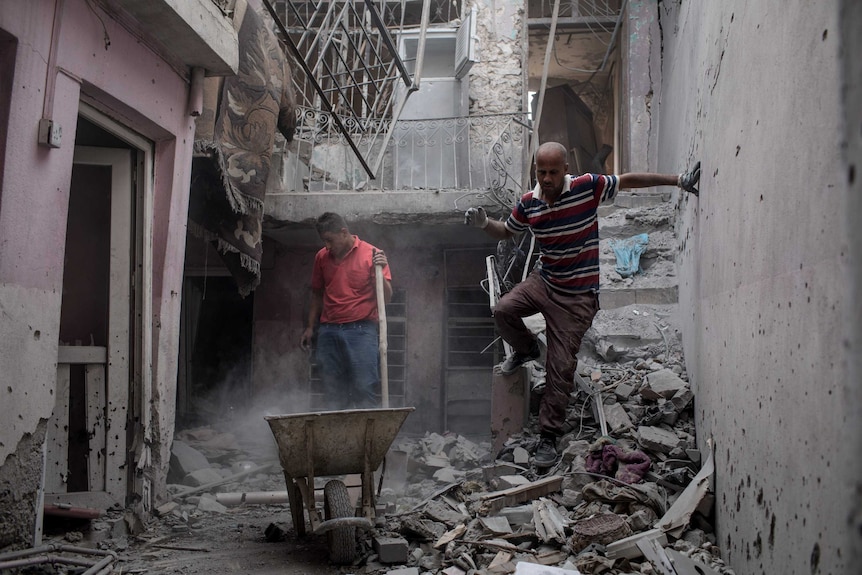 Men clear rubble from a semi destroyed building.