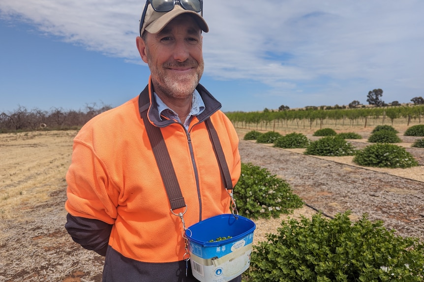 Dave, un hombre de mediana edad de piel clara, con chaqueta de alta visibilidad y gorra, tiene un cordón con un cubo de helado de alcaparras.