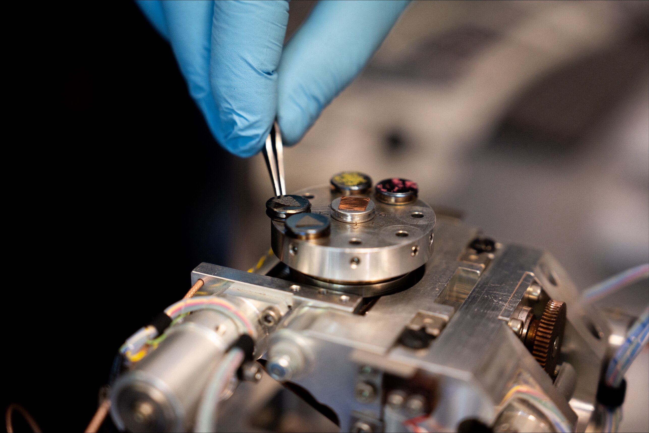 Os dedos enluvados usam uma pinça para colocar uma pequena amostra em um kit de teste de perigo.