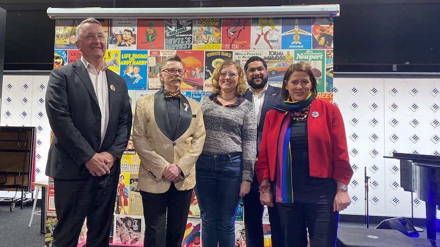 Five people standing facing the camera, in front of a mural. 