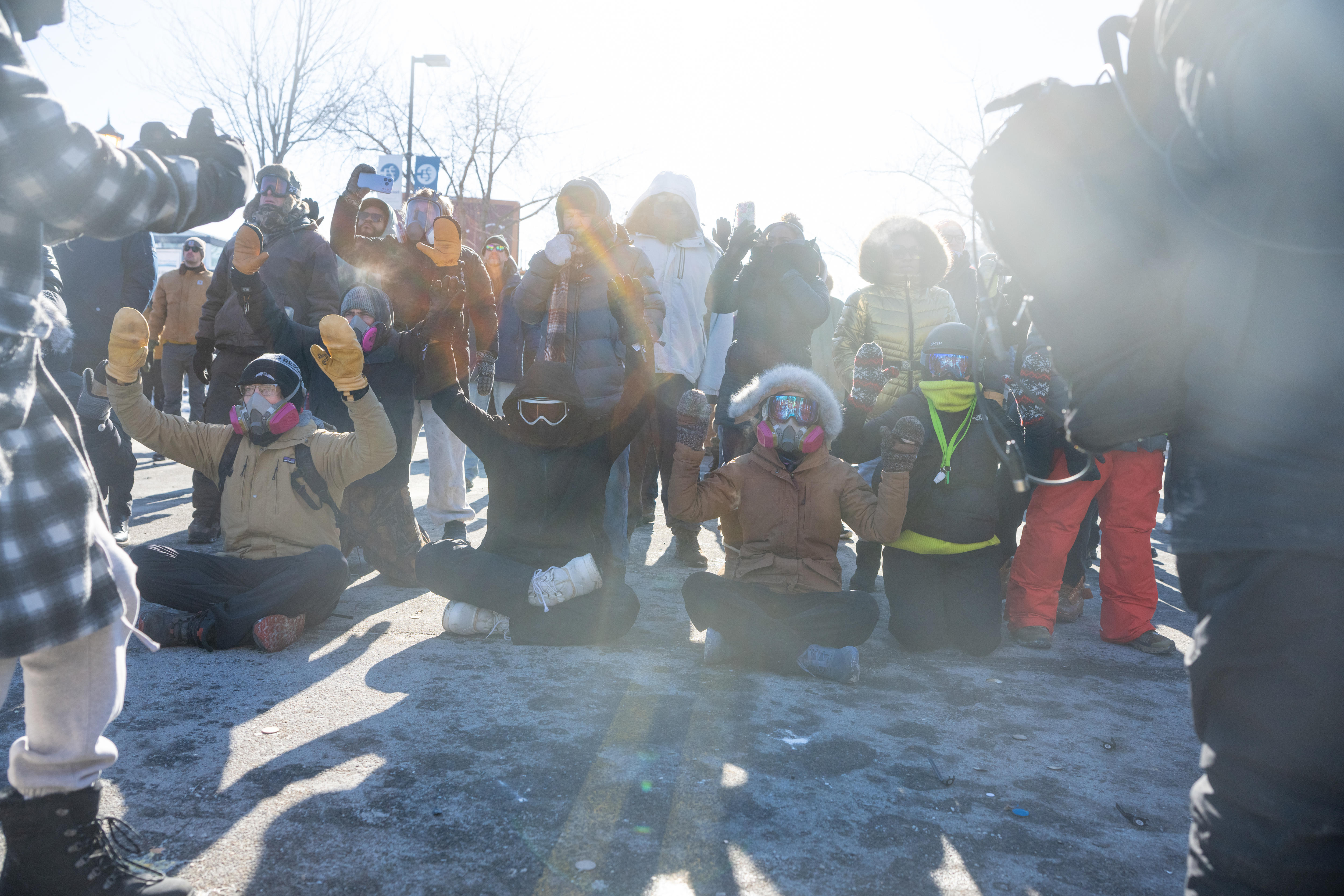 Un grupo de personas con chaquetas de invierno y máscaras se sientan en un suelo cubierto de nieve durante una protesta.