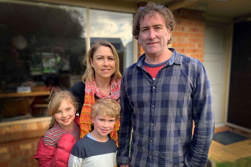 A mother, father, son and daughter stand together outside a red brick home.