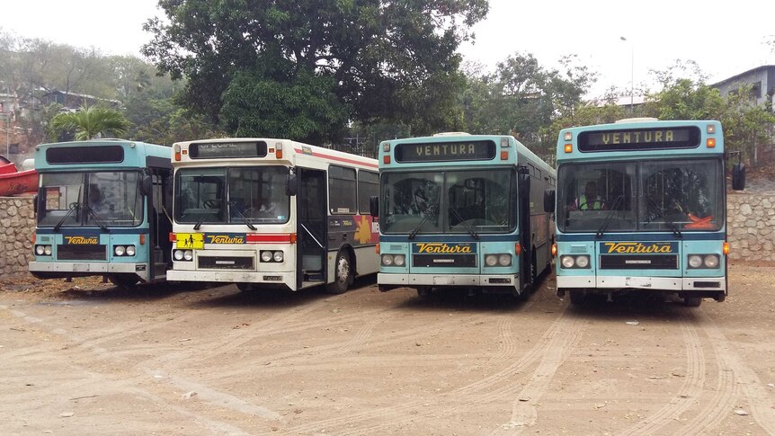 Four older style buses facing the camera with signs saying Ventura rest on a dirt carpark.