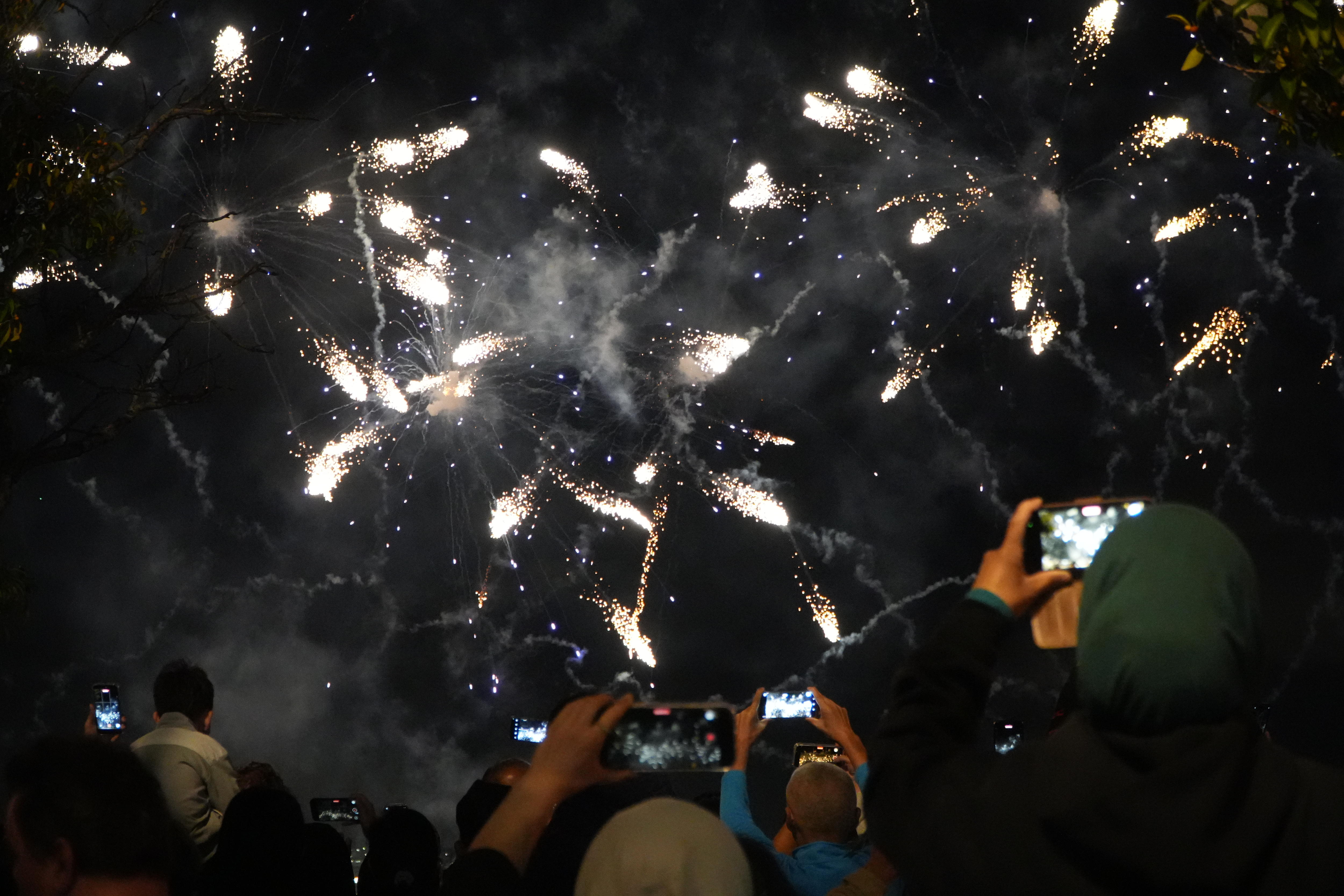 Fogos de artifício explodem no céu enquanto as pessoas gravam com seus telefones