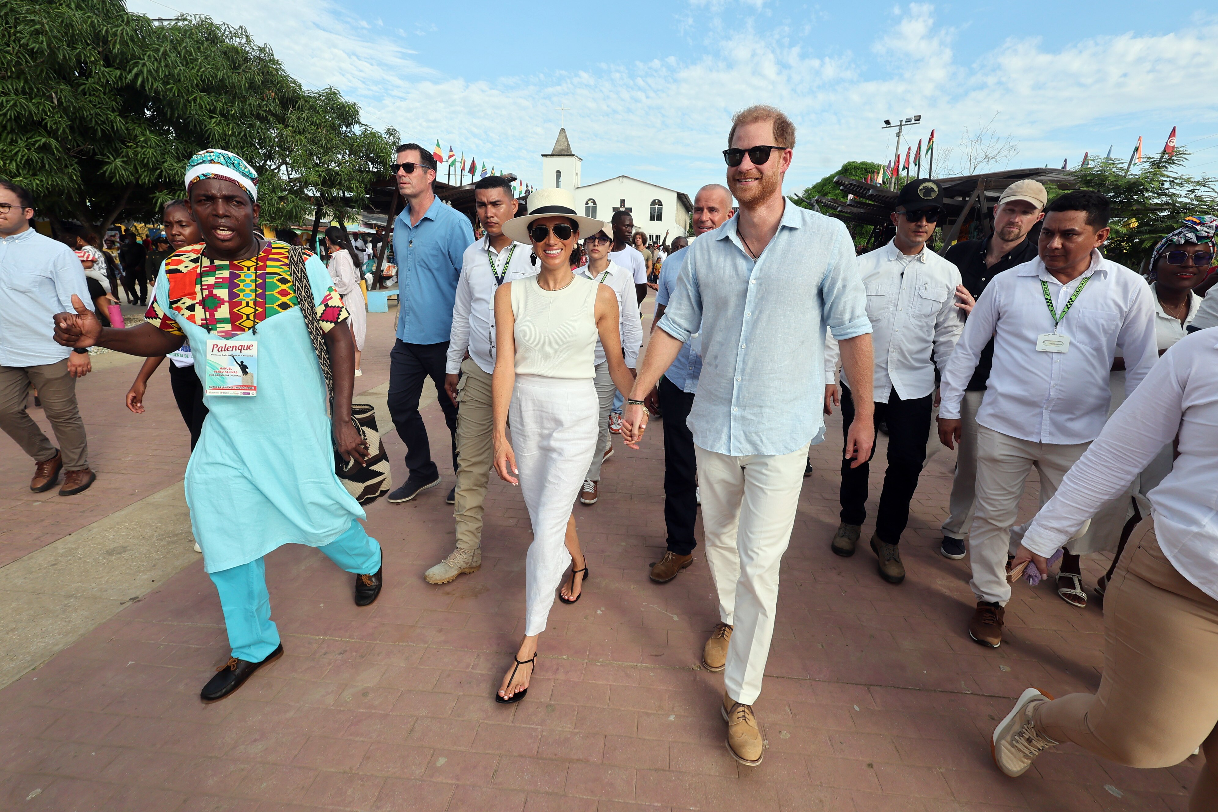 Harry and Meghan smiling and strolling down the streets of a town, surrounded by people.