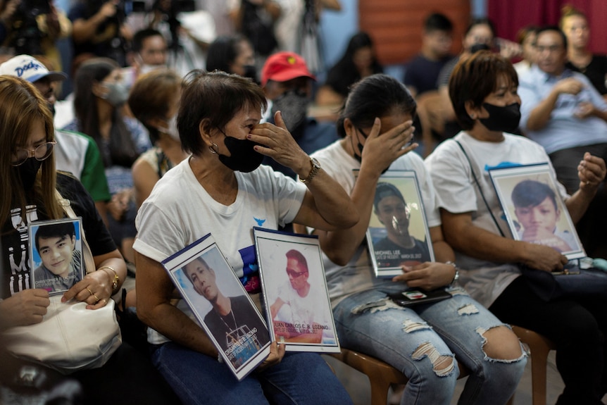Three women wearing white t-shirts hold placards while emotional