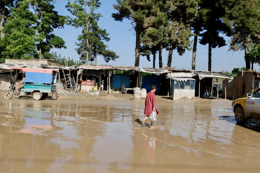 Image of a boy walking along a flooded and muddy street.