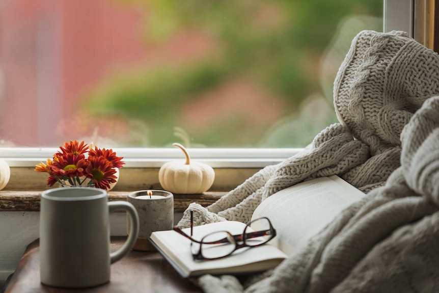 A cosy readying nook with candles ,glasses, a book and a hot drink.