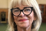 A blonde older woman wearing black glasses