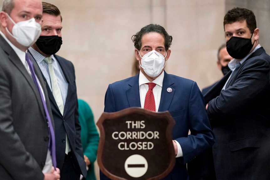 A group of men in masks stand behind a sign that reads "This corridor closed"