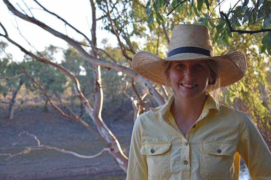 Woman in big hat standing in front of a tree.