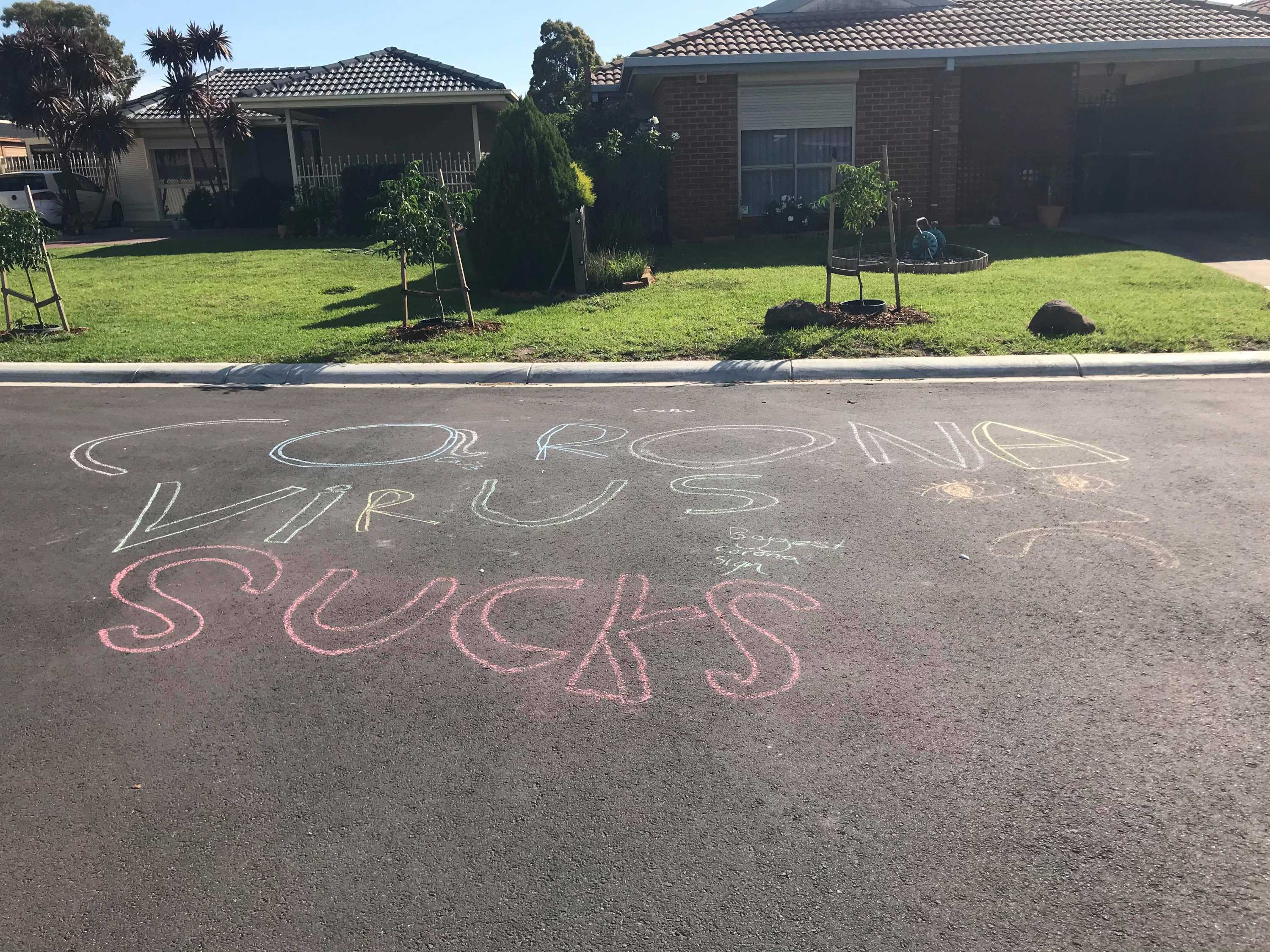 The words "corona virus sucks" in big chalk letters on a suburban street.