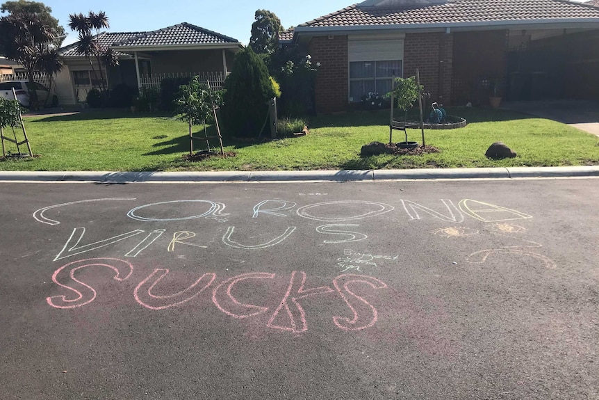 The words "corona virus sucks" in big chalk letters on a suburban street.