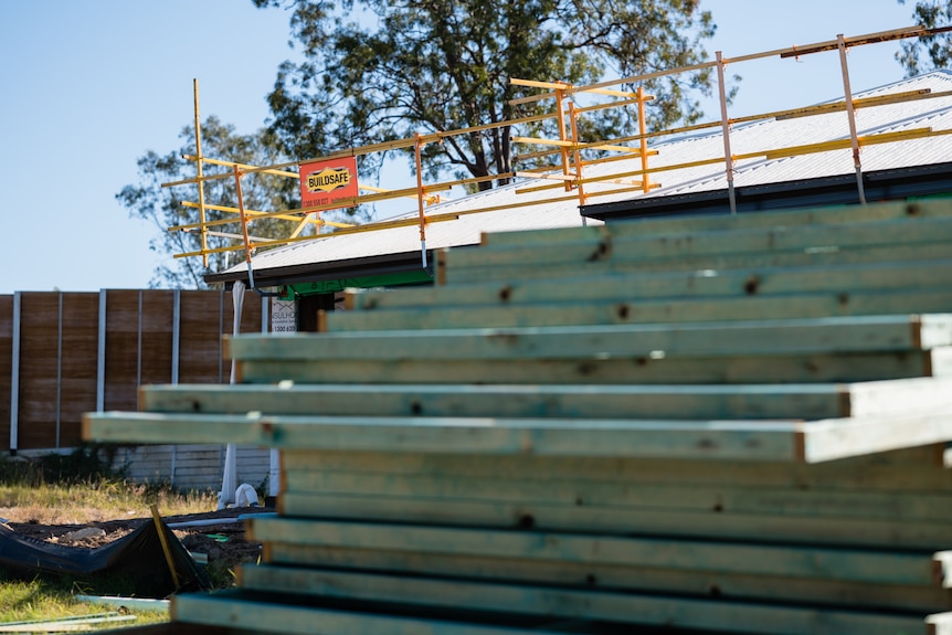 Building materials piled up at a house being built, which can be seen in the background