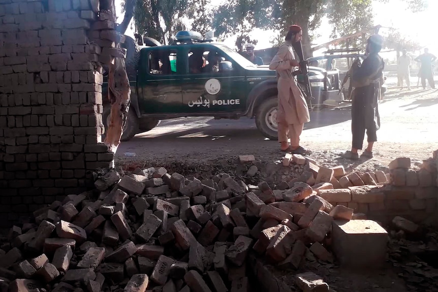 塔利班战士在爆炸现场从外面检查倒塌的墙壁。