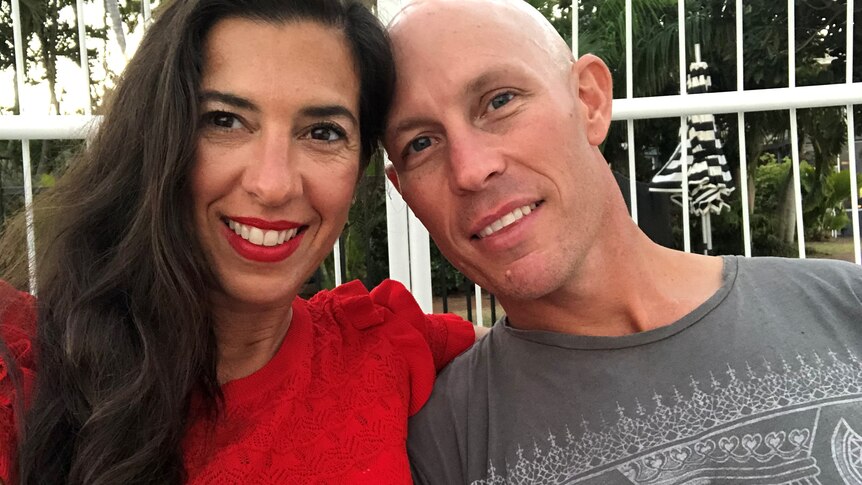 A smiling woman in a red shirt with red lipstick and a man with a grey shirt