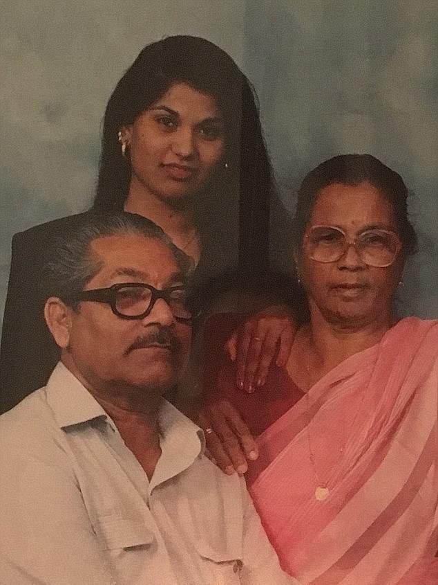 A family of three, mother and father are seated with glasses on, the child in the background with long dark har