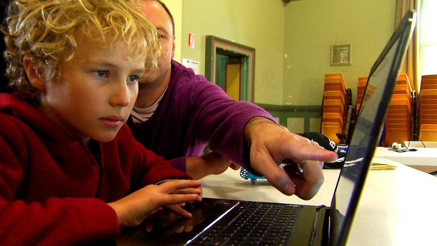 A child looks at a lap top computer. A man sitting next to him points to the screen.
