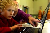 A child looks at a lap top computer. A man sitting next to him points to the screen.