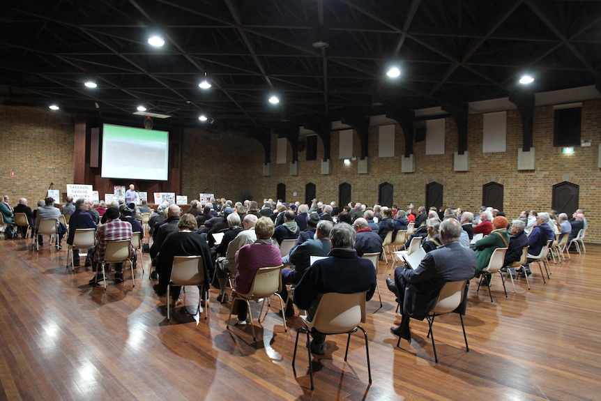 a community hall filled with people sitting in chairs facing a slideshow