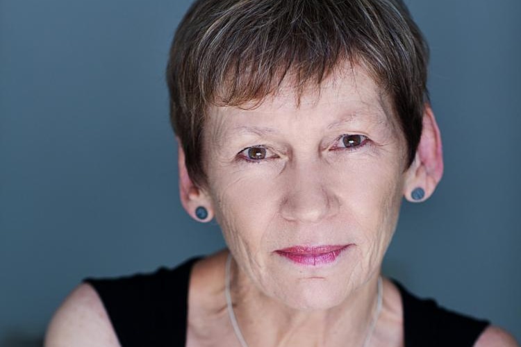 Close-up photo of Kristina Olsson in black singlet, with small, round blue earrings and short hair, smiling slightly.