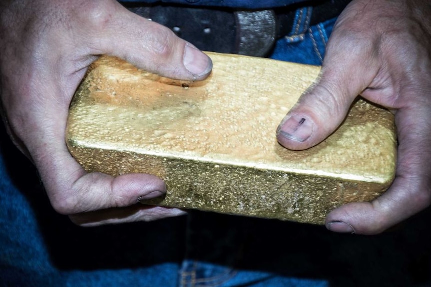 A man holds a bar of gold