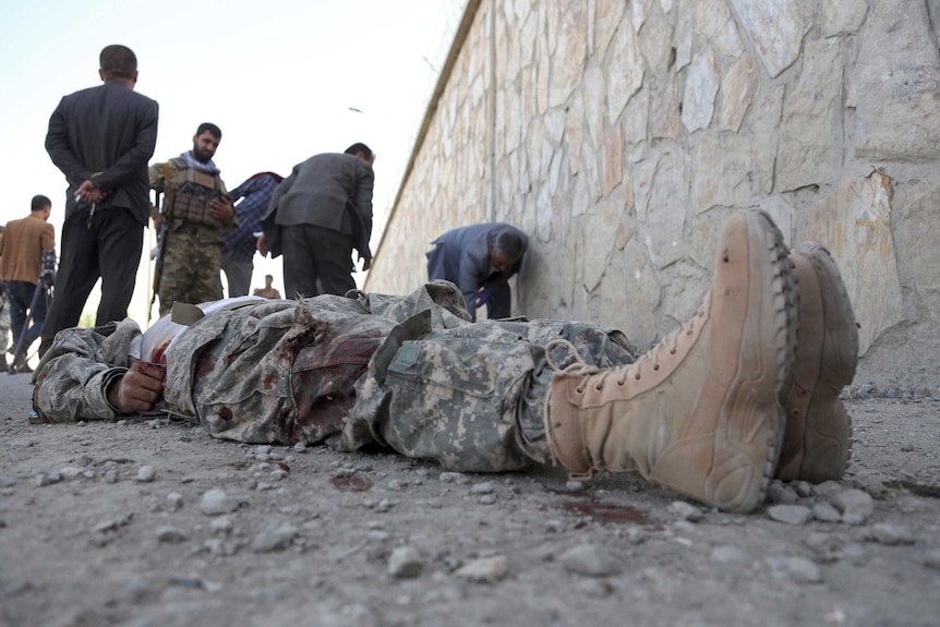 A body in military uniform lies on the ground as officials inspect the scene.