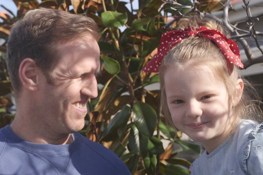 A father holding his smiling daughter who has a red bow in  her hair.