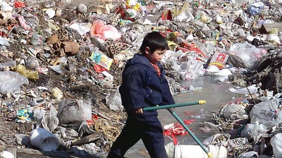 Boy crosses stream in rubbish tip, China