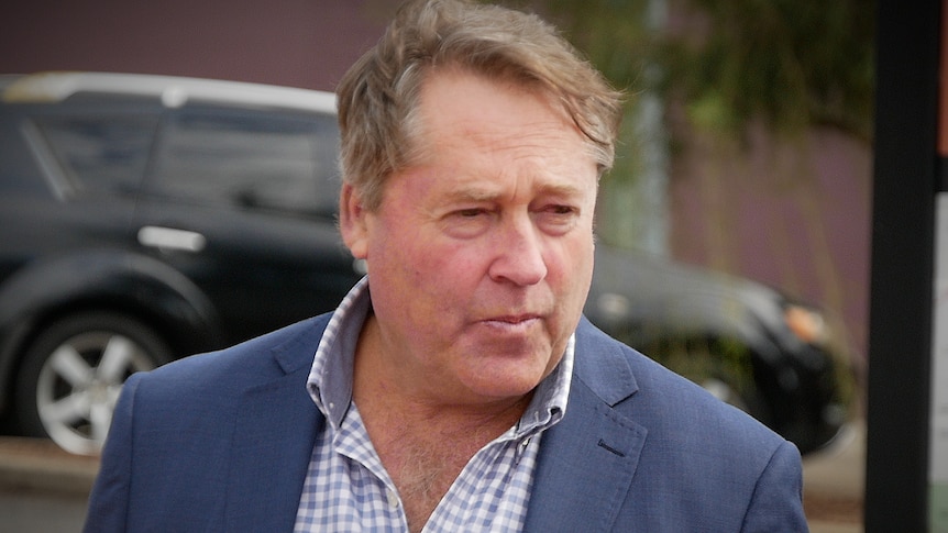 A man in a blue suit and checked shirt walking