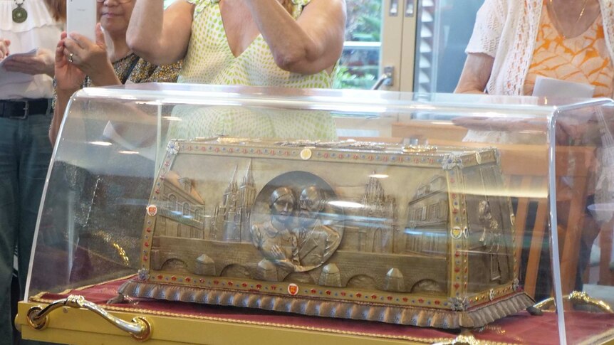 People gathered around a glass case housing an intricate reliquary box made out a bronze like material