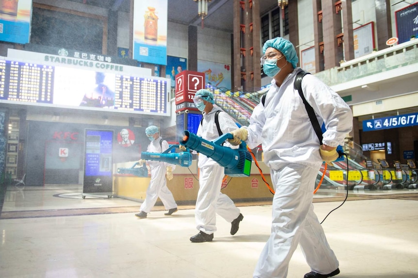 men in white suits and protective equipment spray liquid in a railway station